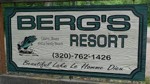 A wooden sign for Berg's Resort features a leaping fish, phone number (320)-762-1426, and the words "Cabins, Boats and a Sandy Beach. Beautiful Lake Le Homme Dieu.
