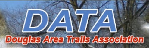 Logo for Douglas Area Trails Association featuring large blue letters "DATA" above the association name in orange text, set against a background of leafless trees and blue sky, highlighting DATA Snowmobile Trails.