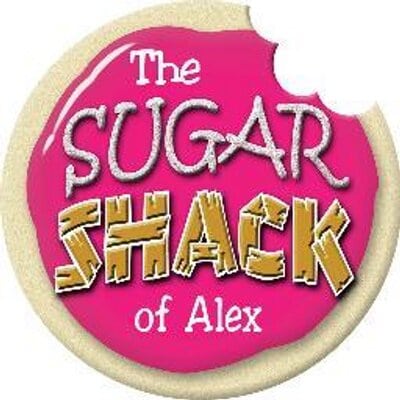 A round cookie with a bite taken out, topped with pink icing featuring "The Sugar Shack" of Alex in white and yellow stylized letters.