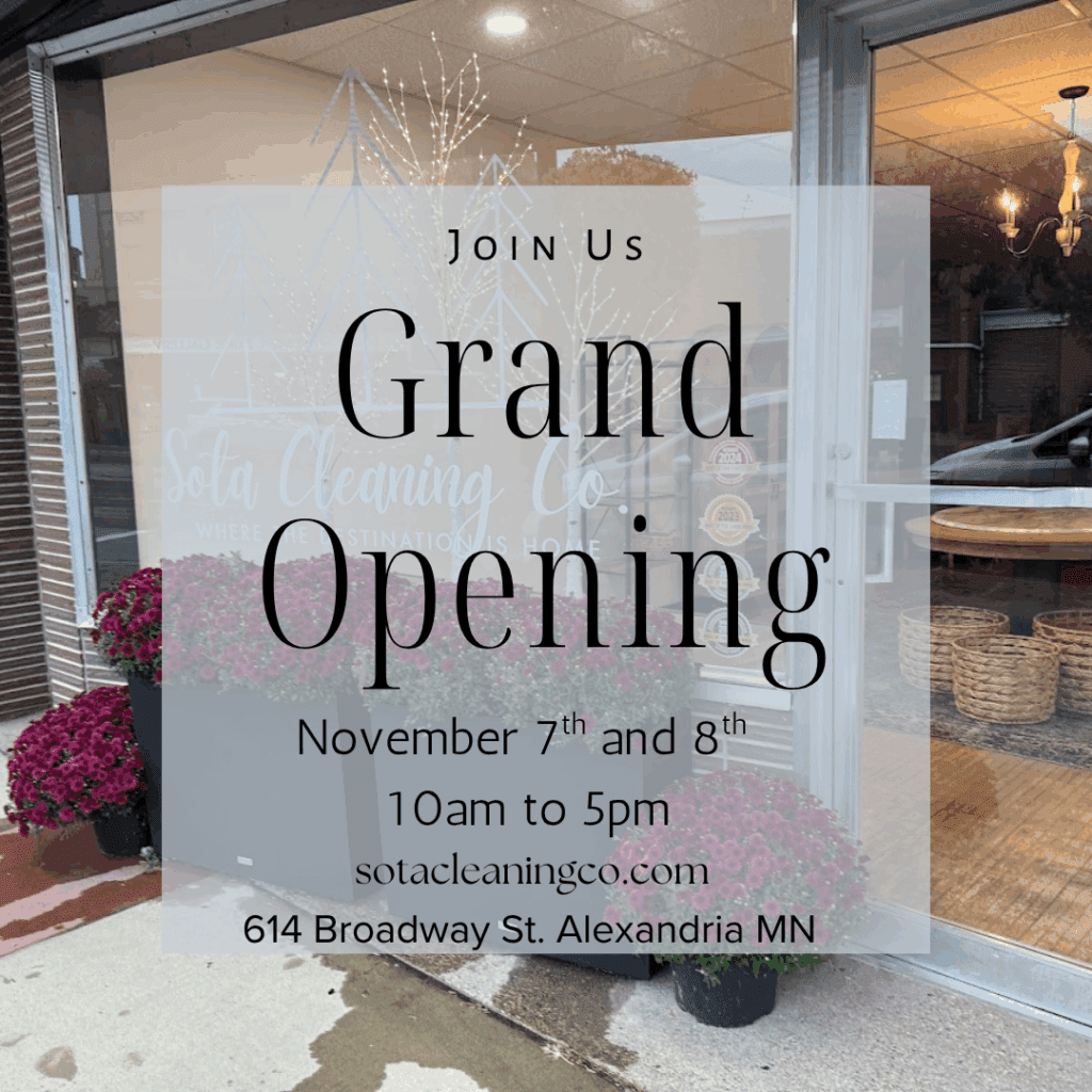 A window sign announces Sota Cleaning Co.'s grand opening of their boutique on November 7th and 8th from 10am to 5pm at 614 Broadway St., Alexandria, MN. Purple flowers and large baskets decorate the storefront.
