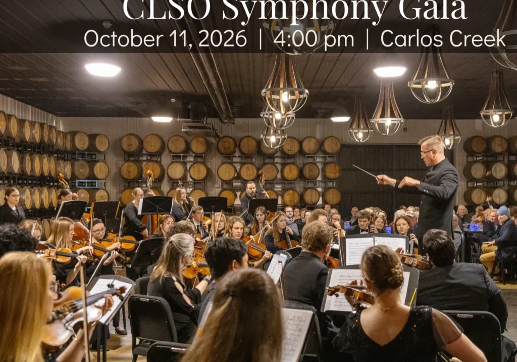 A conductor leads an orchestra in a wine cellar, surrounded by barrels, at the CLSO Symphony Gala. Event details: October 11, 2026, 4:00 pm, Carlos Creek.