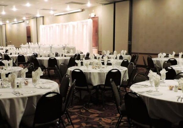 A banquet hall at the Alexandria Hotel set up for an event, with round tables covered in white tablecloths, neatly arranged chairs, and folded napkins at each place setting. The softly lit Conference Center room is beautifully decorated for a formal gathering.