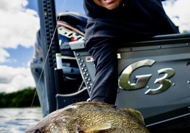 A man on a boat smiles as he holds a large fish over the water, preparing to release it. The boat and sky are visible in the background, with the “World Fishing Network” logo in the top right corner.