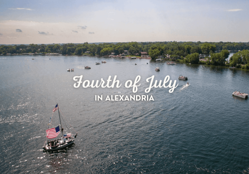 A small boat decorated with American flags floats on a lake in Alexandria, surrounded by other boats and a tree-lined shore. Text reads, "Fourth of July in Alexandria.