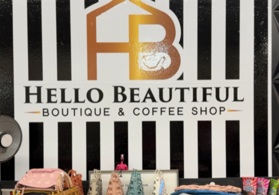 Hello Beautiful. A boutique counter displays bags, accessories, and a tumbler before a black-and-white striped wall with a gold “Hello Beautiful” logo and the text: “Hello Beautiful Boutique & Coffee Shop.”.