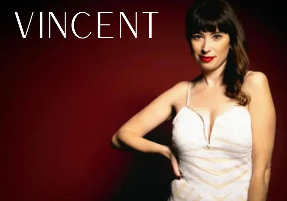 A woman in a white dress with wavy dark hair stands against a dark red background, capturing the spirit of live performance. "LESLIE VINCENT" appears in large white letters in the top left corner, evoking the magic of Theatre L'Homme Dieu.