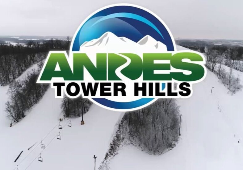 Logo for Andes Tower Hills featuring snowy mountains and stylized text, overlaid on a winter landscape with snow-covered hills, ski lifts, and trees—highlighting the excitement of skiing adventures in the background.