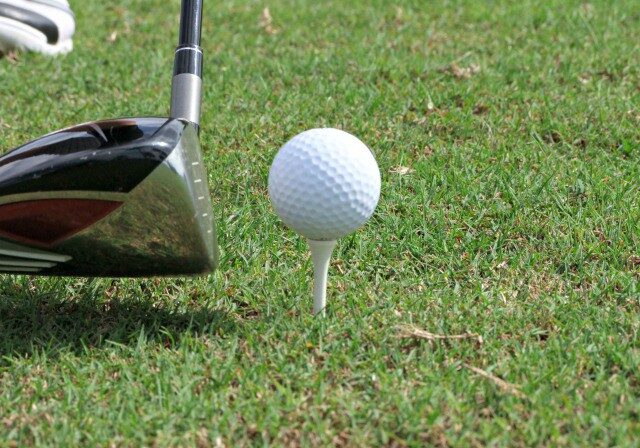 A close-up of a golf club positioned next to a white golf ball on a tee, ready for a shot on green grass—perfect inspiration for your next Autumn Golf Get-Away.