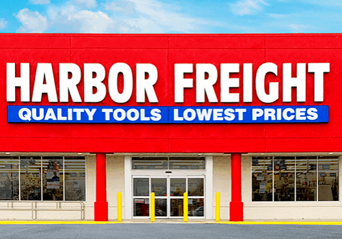 The front of a Harbor Freight store features bold red Harbor Freight signage and a blue banner stating "Quality Tools Lowest Prices" above the main entrance.