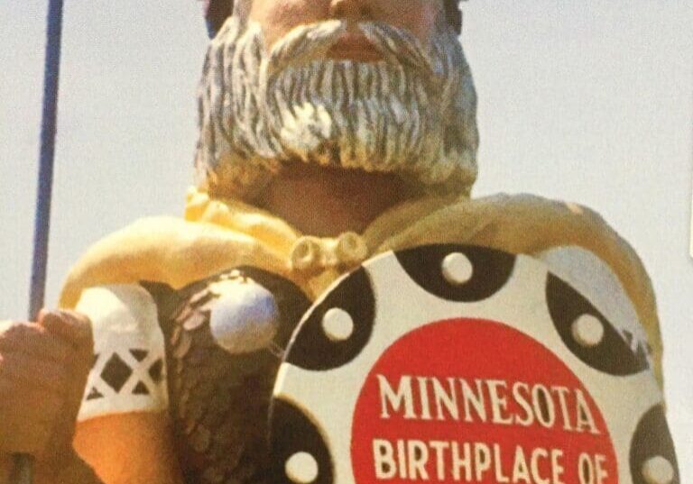 Statue of Big Ole, a Viking with a helmet and shield reading “Minnesota Birthplace of America?” The Viking has a blonde beard, wears armor, and stands proudly under a clear sky—perfect for celebrating his happy 50th birthday.